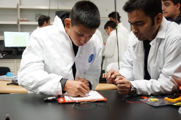Two students in lab coat working on project